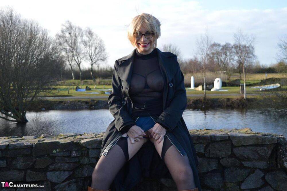 Mature blonde Barby Slut exposes her tits and twat in leather coat by a river - #9