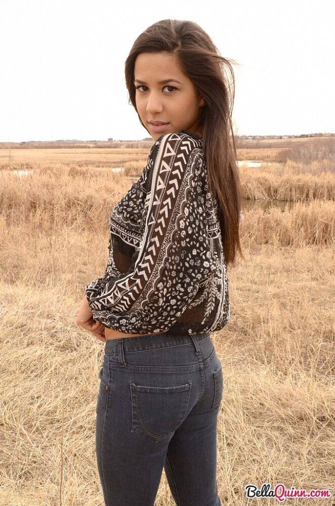 Latina girl Bella Quinn models in a field wearing a bra and jeans | Photo: 1862669