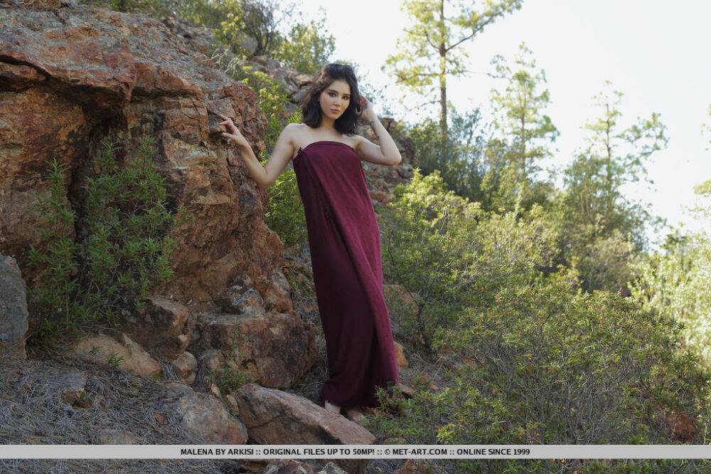 Barefoot teen Malena slips off a long dress to pose nude on a rocky bank - #13