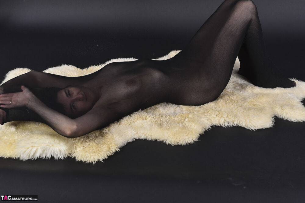 Naked mature woman encases herself in a stocking atop a rug - #1