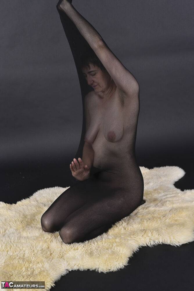 Naked mature woman encases herself in a stocking atop a rug - #2