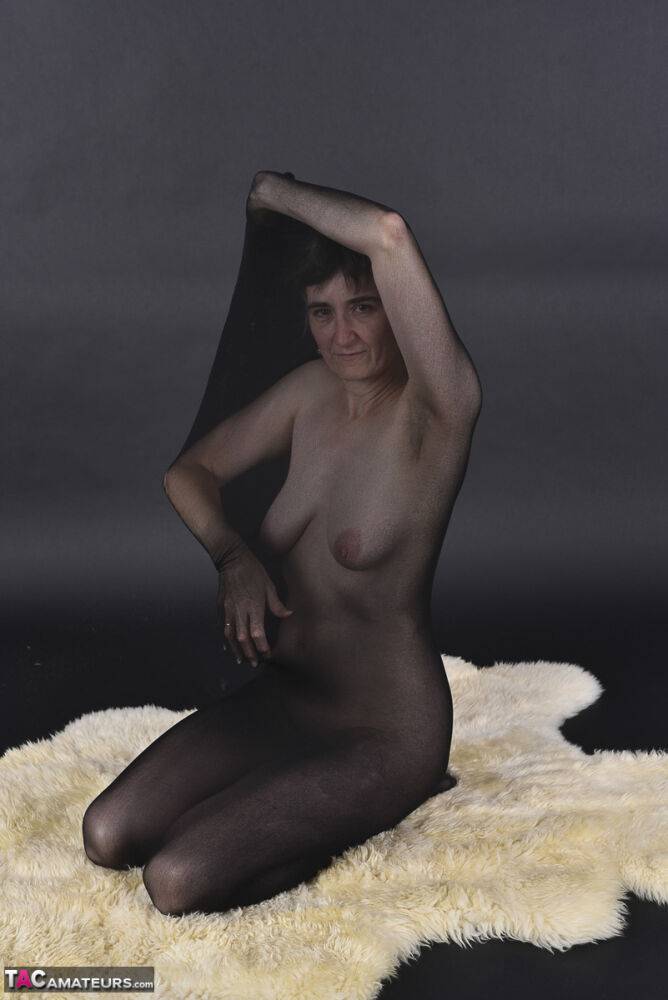 Naked mature woman encases herself in a stocking atop a rug - #14