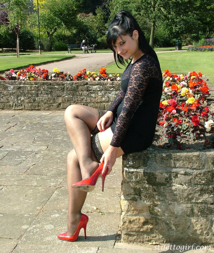 Brunette female in a short dress and stockings dangles red heels on stone wall - #9