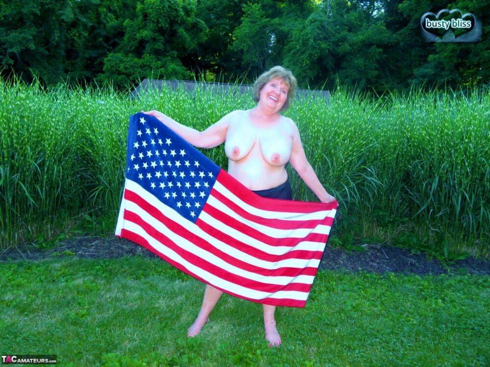 Older plumper Busty Bliss holds an American flag while totally naked in a yard - #9