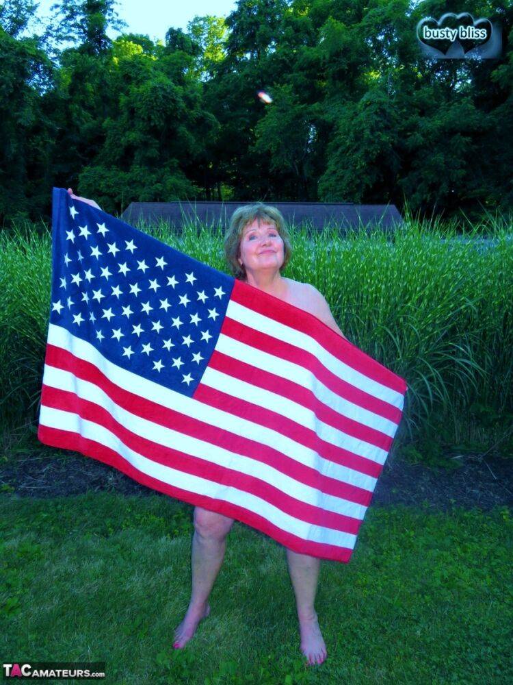 Older plumper Busty Bliss holds an American flag while totally naked in a yard - #5