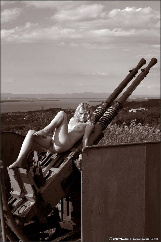 Blonde model poses totally naked atop an artillery gun in a field - #1