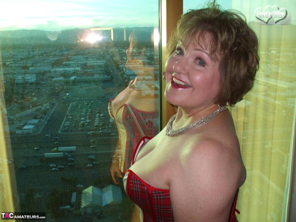 Mature woman Busty Bliss looses her big tits from a corset by her condo window - #1