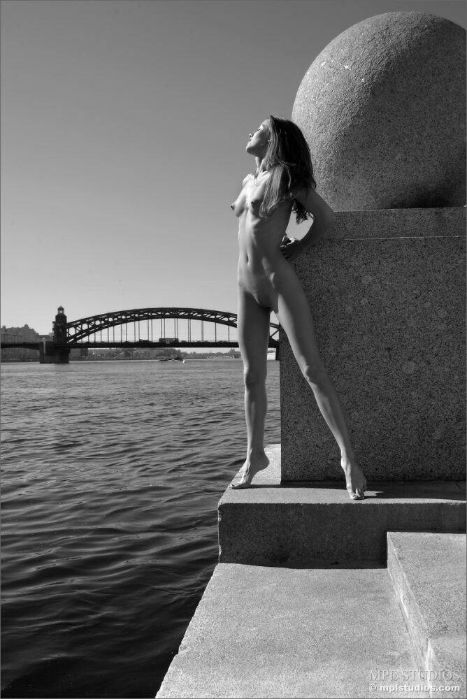 Skinny girl models completely naked near a landmark by a river - #11