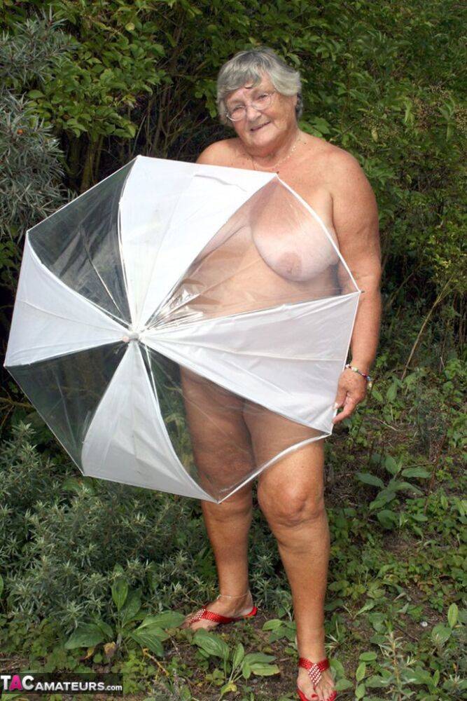 Obese oma Grandma Libby holds an umbrella while posing naked by fir trees - #9