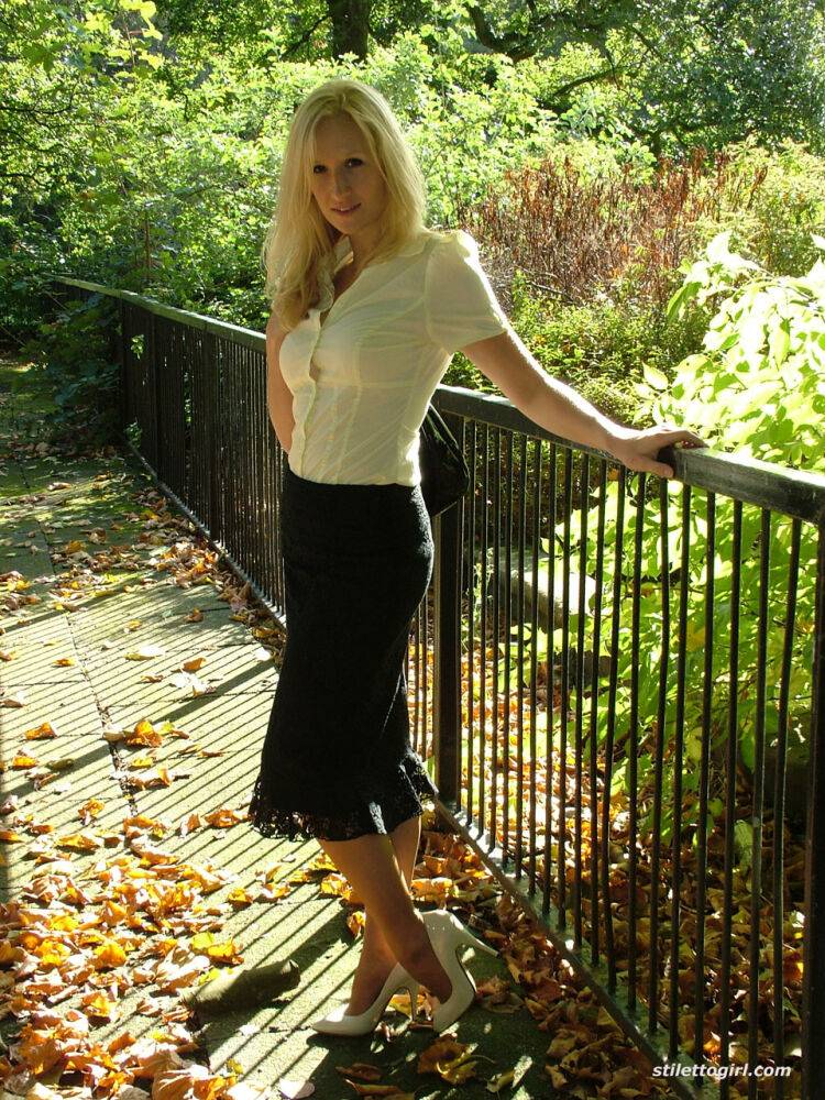 Clothed blonde Iona shows off her white stilettos in a long skirt by a park - #7