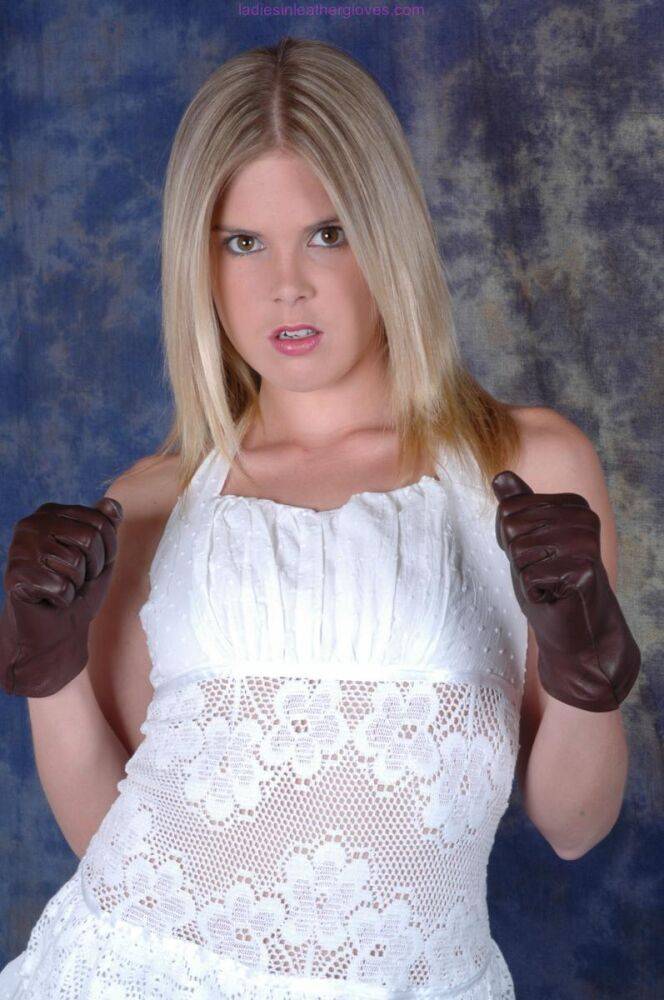 Blonde female pulls on brown leather gloves while wearing a white dress - #1