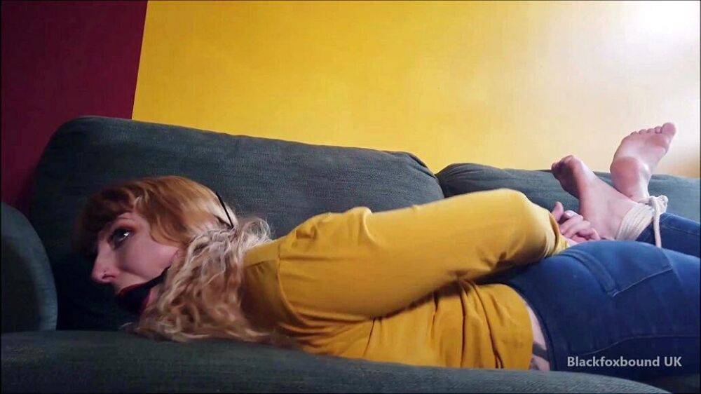 Barefoot white girl is hogtied on a sofa while ball gagged in her clothing - #15