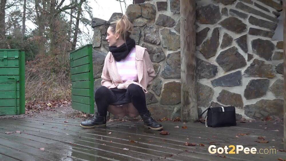 White girl Cynthia Vellons takes a piss on a deck behind a stone structure - #4