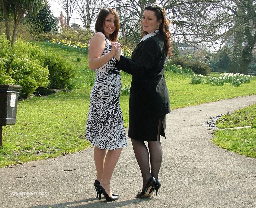 Clothed ladies hold hands while showing their spiked heels on a walking path - #7