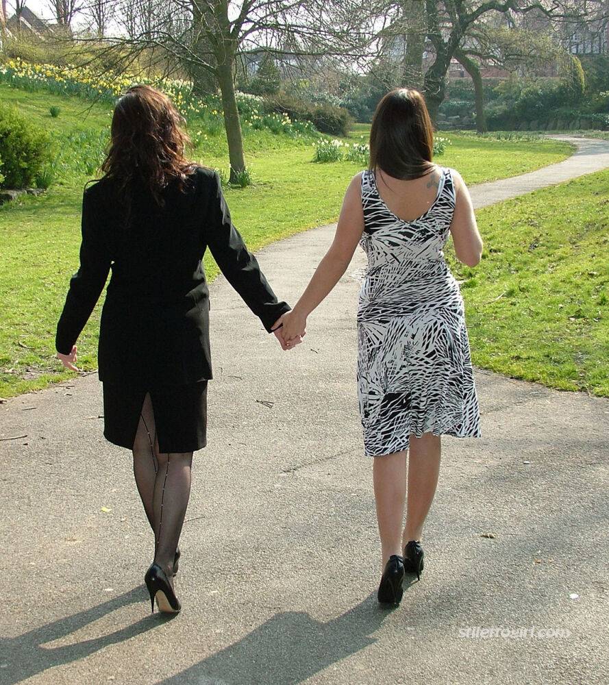 Clothed ladies hold hands while showing their spiked heels on a walking path - #8