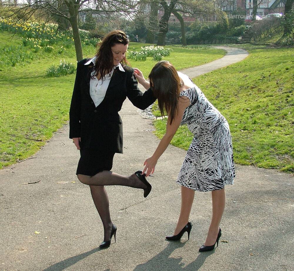 Clothed ladies hold hands while showing their spiked heels on a walking path - #3