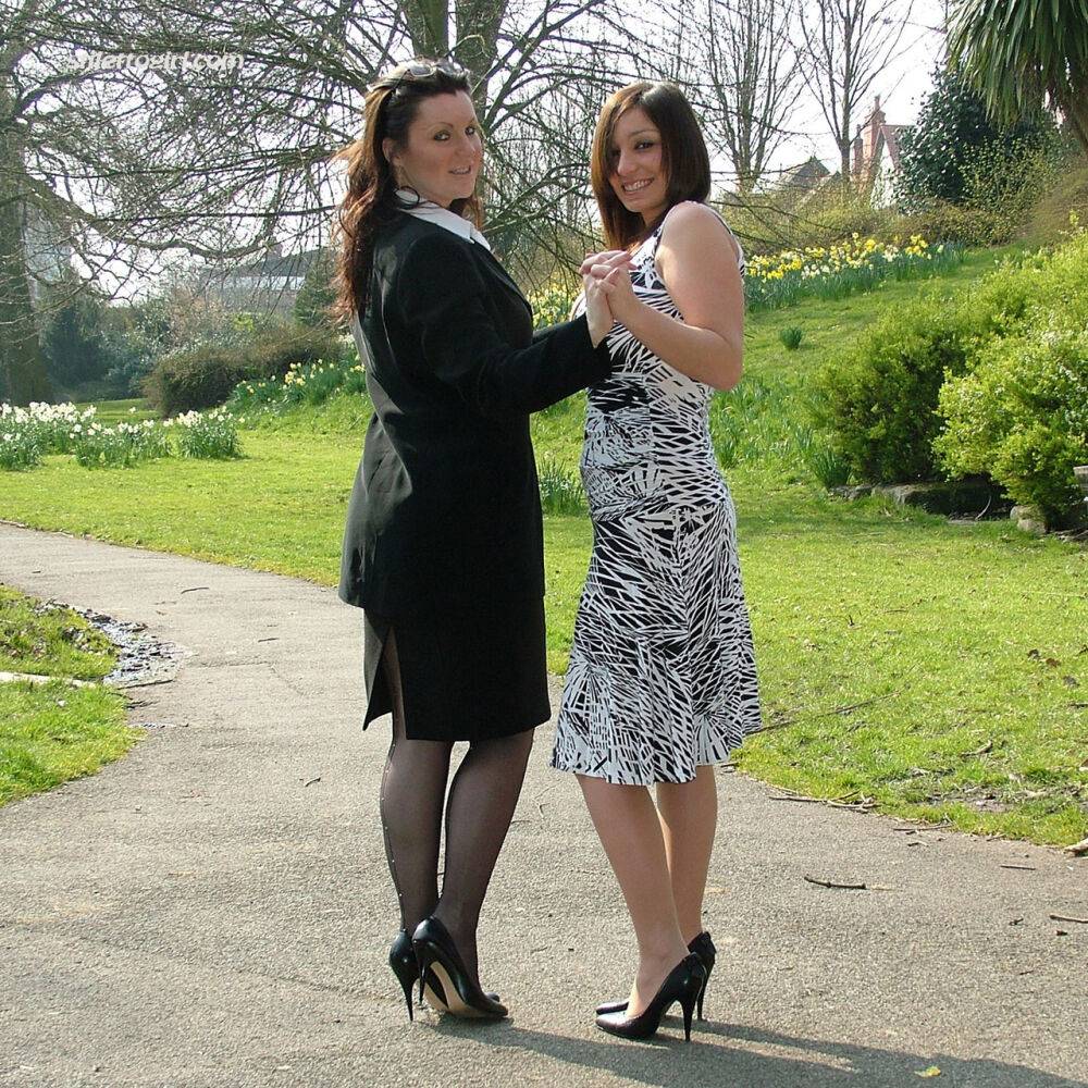 Clothed ladies hold hands while showing their spiked heels on a walking path - #4