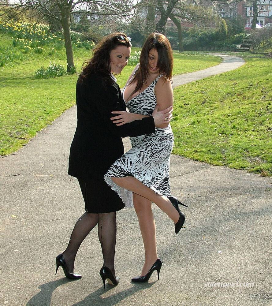 Clothed ladies hold hands while showing their spiked heels on a walking path - #9