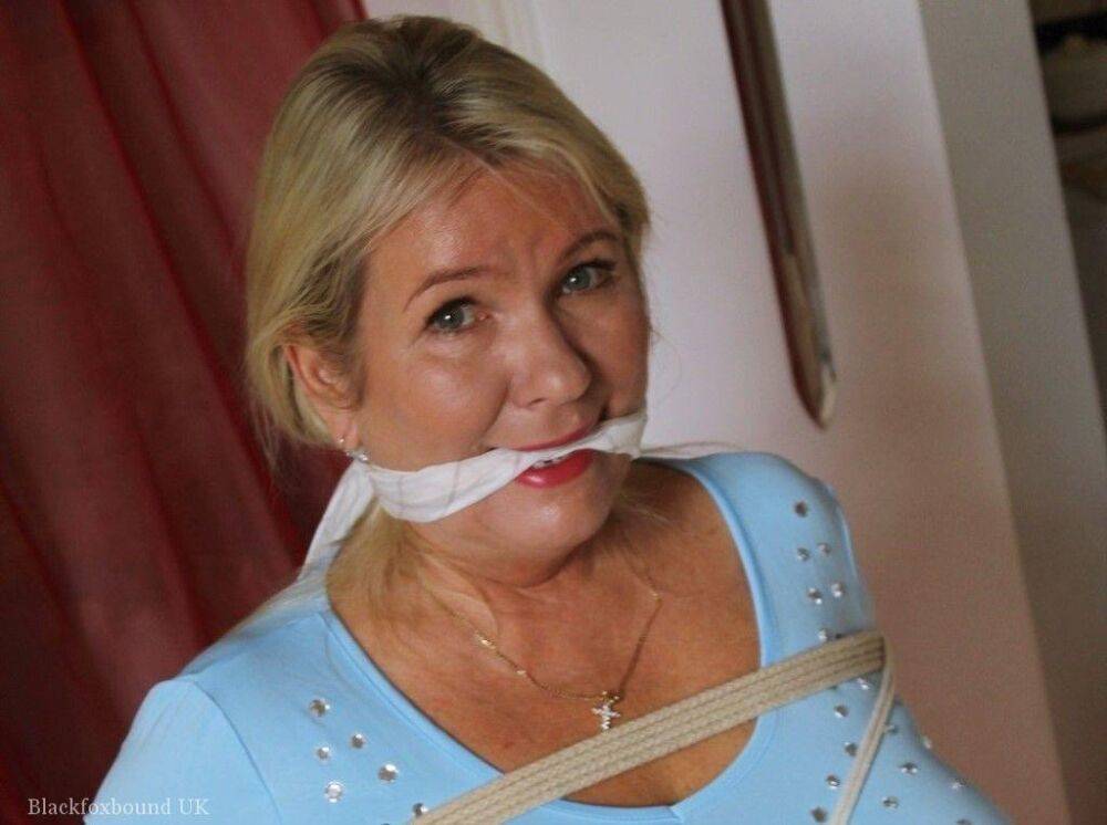 Older blonde is gagged and tied up in a variety of outfits inside her house - #12