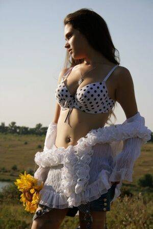 Young brunette Ira I holds sunflowers while stripping totally naked in a field on nudesceleb.com