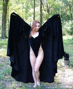 Redhead amateur Amber Lily models nude in a forest draped in a black cape on nudesceleb.com