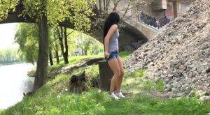 Dark haired traveler Lexi looks for a place to pee and pisses under a bridge on nudesceleb.com