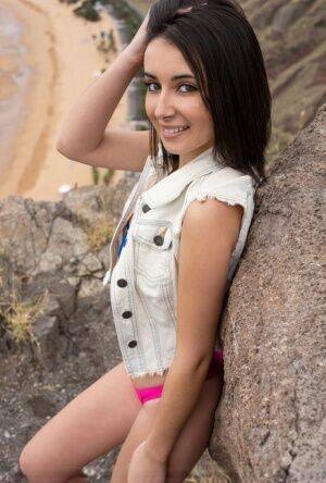 Petite teen Dionisia doffs a denim vest and bikini to model nude on a cliff on nudesceleb.com