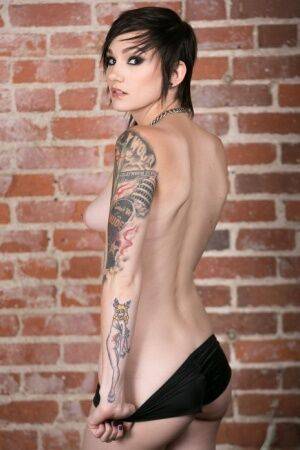 Punk girl Nikki Hearts frees her tattooed body of clothes afore a brick wall on nudesceleb.com