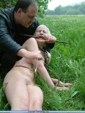 Naked blonde slave is caned and stomped on in a field of lush grass on nudesceleb.com