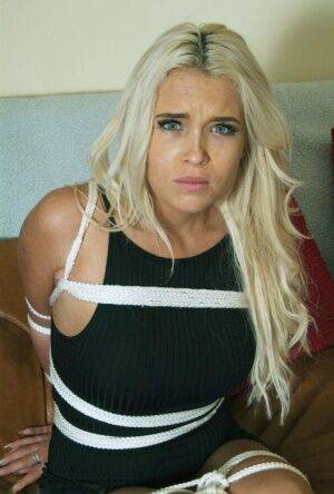 White female with long blonde hair is tied up with rope in a black dress on nudesceleb.com