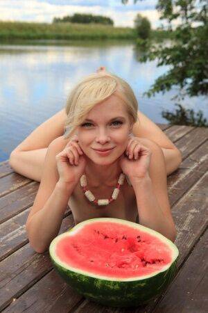 Beautiful blonde Feeona eats a watermelon while posing naked on lakeside dock on nudesceleb.com