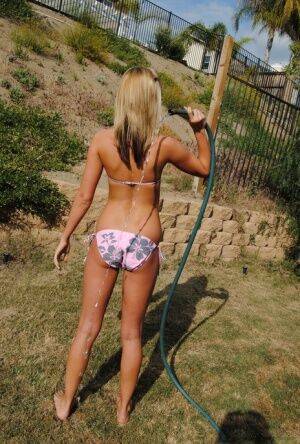 Young blonde girl in a bikini soaks herself with a garden hose on nudesceleb.com