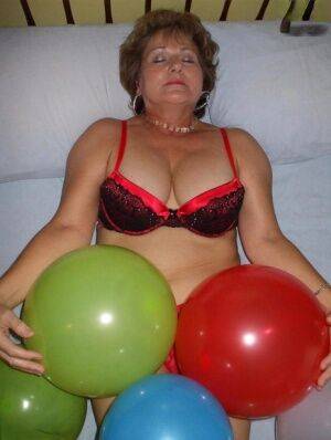 Mature woman Busty Bliss goes topless on her bed while playing with balloons on nudesceleb.com