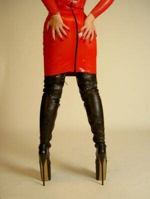 Blonde chick Avengelique models a red latex dress in thigh-high stiletto boots on nudesceleb.com