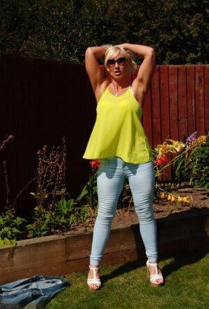 Middle-aged blonde Melody models in a bra and faded jeans in a backyard on nudesceleb.com