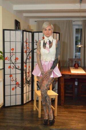 Tattooed platinum blonde Miss Francine models a raincoat over a latex dress on nudesceleb.com