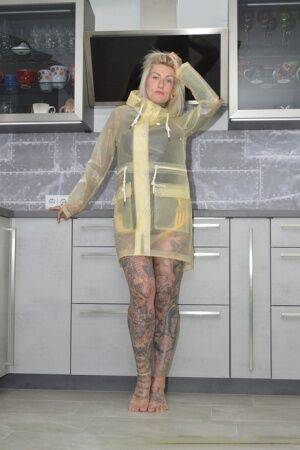 Tattooed blonde Miss Francine models barefoot in a raincoat over rubber wear on nudesceleb.com