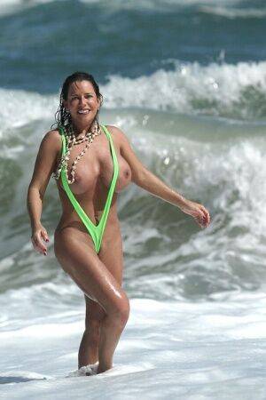 Amply endowed female Alicia Dimarco struts in a v-bikini amid foamy surf on nudesceleb.com