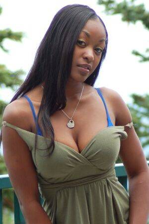Ebony amateur Amber releases her big tits from a long dress on a balcony on nudesceleb.com