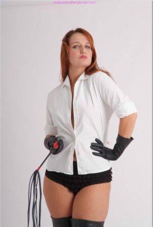 Pale redhead flexes a flogger while wearing black leather gloves and boots on nudesceleb.com