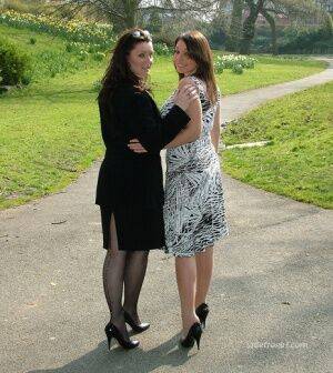 Clothed ladies hold hands while showing their spiked heels on a walking path on nudesceleb.com