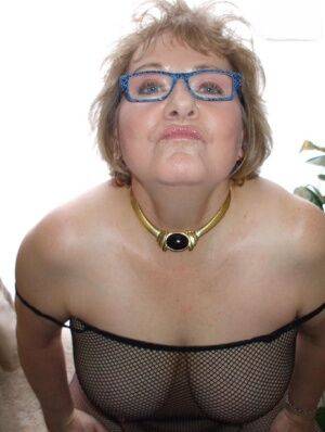 Mature woman Busty Bliss models a mesh bodystocking and glasses on nudesceleb.com